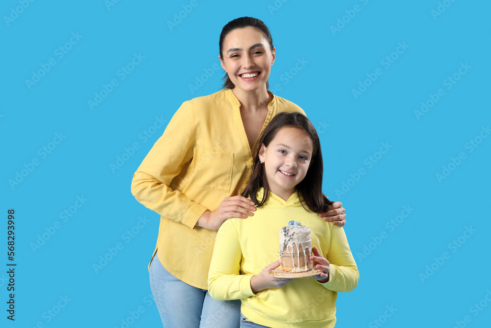 Beautiful woman and her little daughter with Easter cake on blue background Beautiful woman and her little daughter with Easter cake on blue background