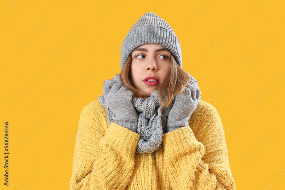 Frozen young woman in winter clothes on yellow background Frozen young woman in winter clothes on yellow background