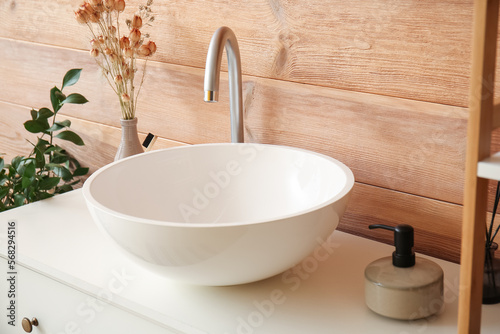 Ceramic sink, vase with dried flowers and bath accessories on drawers in bathroom