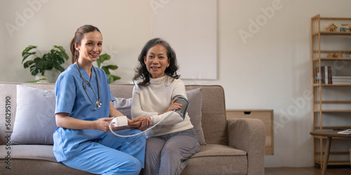 Happy senior woman having her blood pressure measured in a nursing home by her caregiver. Happy nurse measuring blood pressure of a senior woman in living room