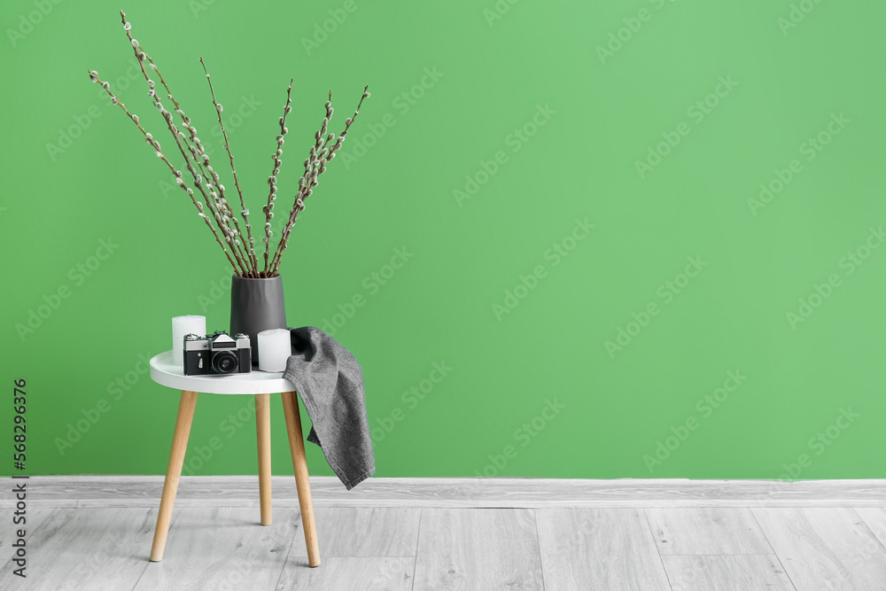 Vase with willow branches, photo camera and candles on table near green wall Vase with willow branches, photo camera and candles on table near green wall