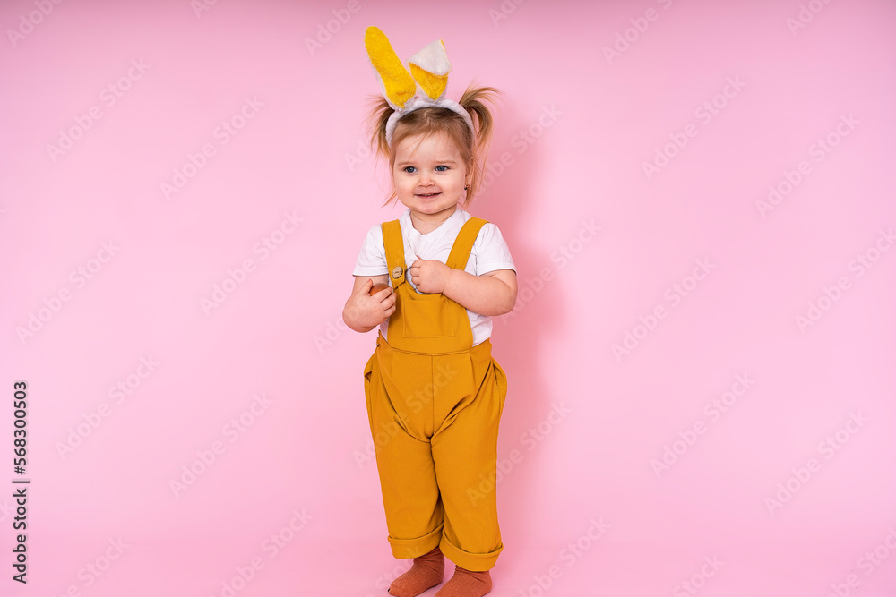 A cheerful girl with rabbit ears on her head and painted eggs in her hands on a pink background. Funny, insanely happy child. Easter for a child.