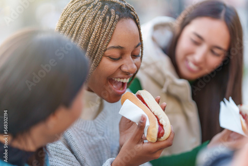 African woman eating hot dog with friends in a park