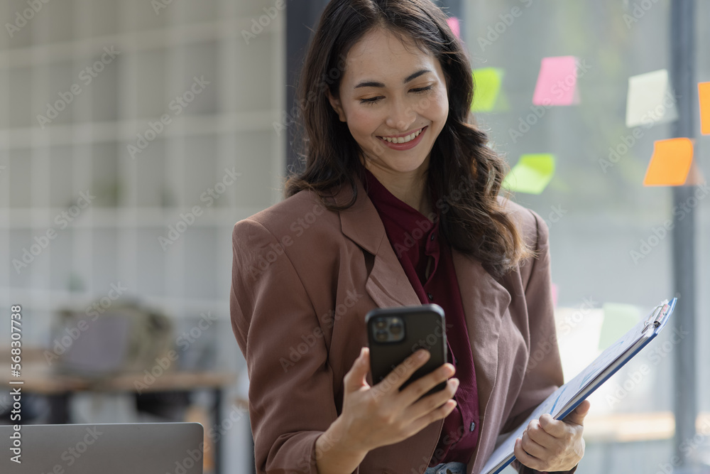 Happy smiling young asian business woman using a smartphone standing in the office, Company worker woman. Happy smiling young asian business woman using a smartphone standing in the office, Company worker woman.