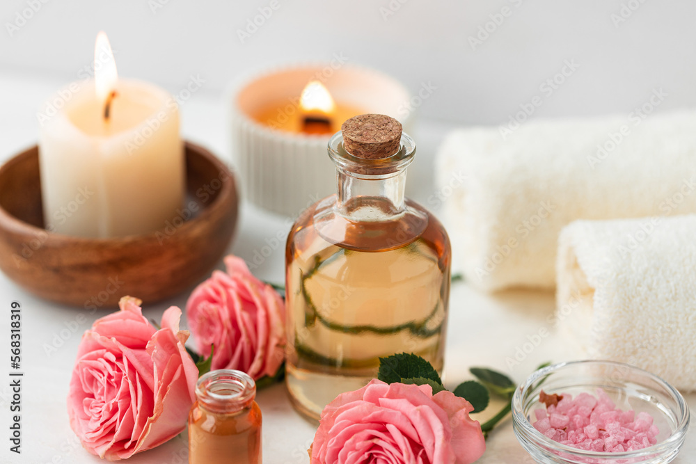 Aromatherapy. Concept of pure organic essential rose oil. Elixir with plant based floral or herbal ingredients. Pink flowers extract. Spa atmosphere with candle, towel. White background Aromatherapy. Concept of pure organic essential rose oil. Elixir with plant based floral or herbal ingredients. Pink flowers extract. Spa atmosphere with candle, towel. White background