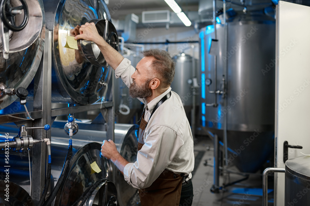 Male brewer making notes on the tanks during brewing process