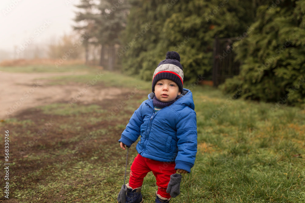 Small boy standing on grass in winter clothes in foggy weather Small boy standing on grass in winter clothes in foggy weather