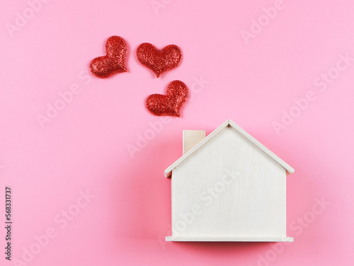 flat lay of wooden model house with red glitter hearts on pink  background. dream house , home of love, strong relationship, valentines.