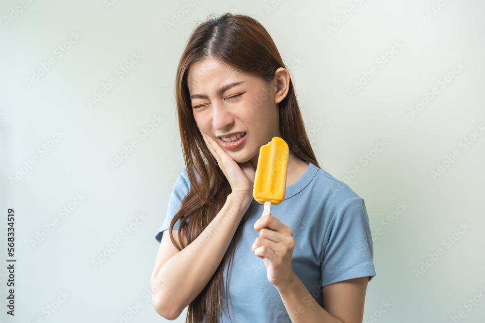 Face expression suffering from sensitive teeth and cold, asian young woman, girl feeling hurt, pain eating ice cream, lolly. Toothache molar tooth at home, dental problem isolated on white background. Face expression suffering from sensitive teeth and cold, asian young woman, girl feeling hurt, pain eating ice cream, lolly. Toothache molar tooth at home, dental problem isolated on white background.