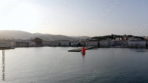 aerial drone shot of molo audace in trieste with red  sailboat passing by 