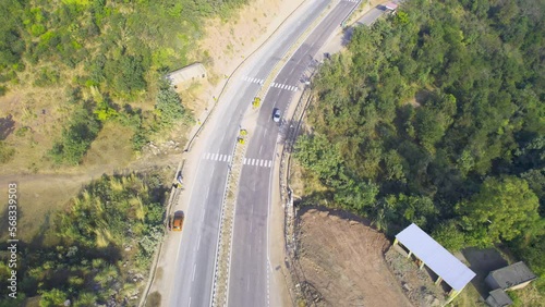 locked aerial drone shot showing car sanding on wide 4 lane highway in hills surrounded by forests and mountains in himachal pradesh on route to manali photo