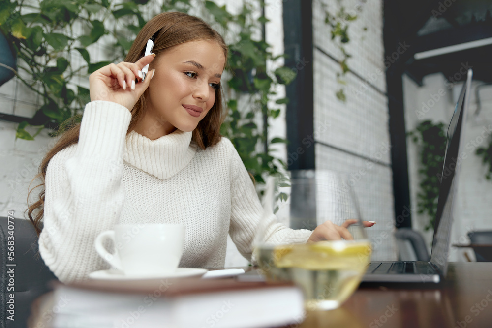 woman sitting at table studying using laptop reading a book. Girl takes a break holding mobile phone surfing internet. woman sitting at table studying using laptop reading a book. Girl takes a break holding mobile phone surfing internet.