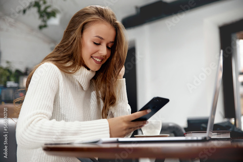 Image of beautiful woman smiling and using cellphone. Girl working with laptop.