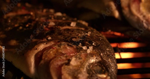Fresh whole fish grilling tastily over the glowing coals of a night barbecue in Slow Motion photo