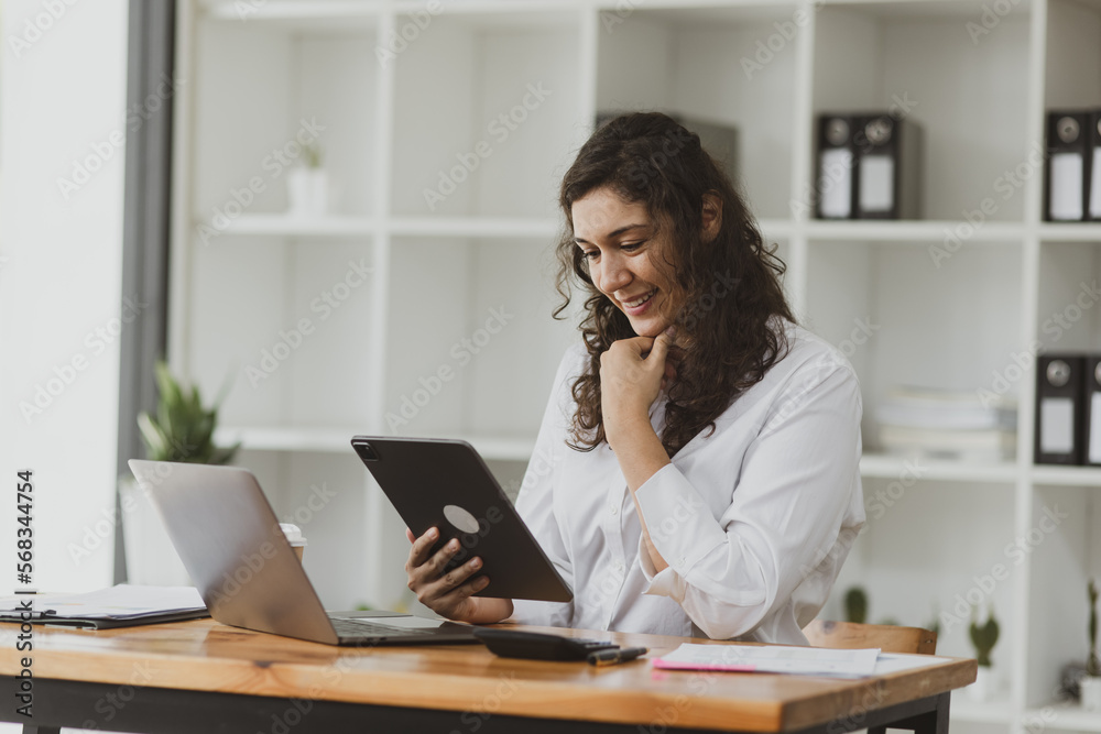 Businesswoman using tablet and laptop computer working at desk in office.
