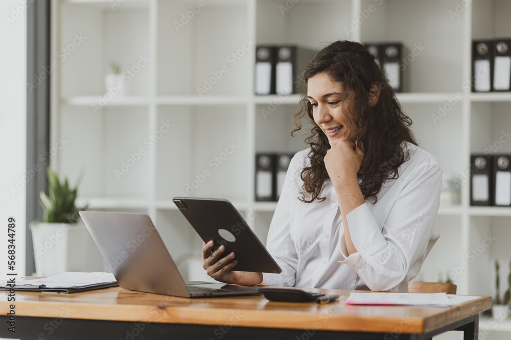 Businesswoman using tablet and laptop computer working at desk in office. Businesswoman using tablet and laptop computer working at desk in office.