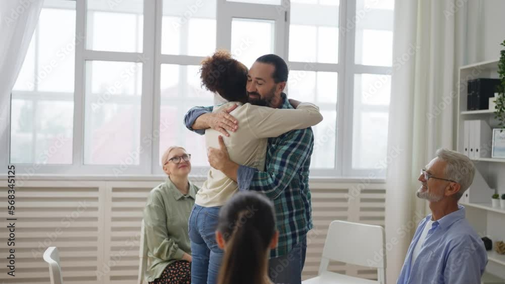 Support group session, two members hug each other, people share their experience Support group session, two members hug each other, people share their experience