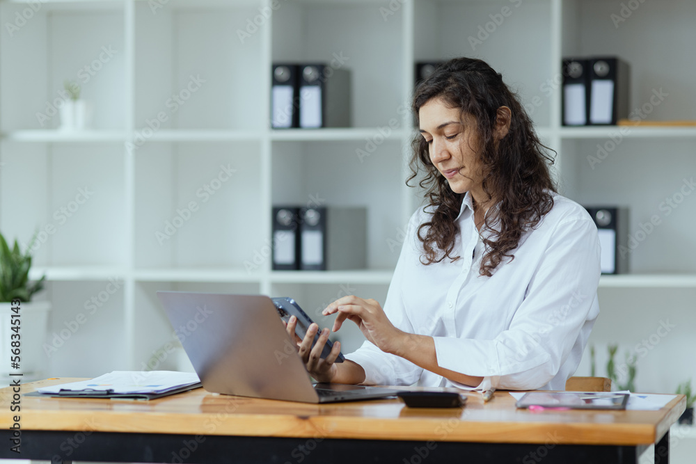 Businesswoman using smartphone and laptop computer working at desk in office. Businesswoman using smartphone and laptop computer working at desk in office.