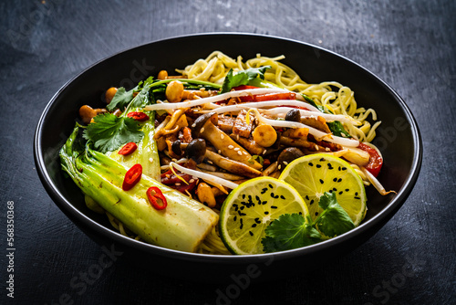 Asian food - Chow Mein noodles, stir fried vegetables, soy sauce and shimeji mushrooms on wooden table
