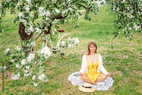 young woman is sitting in a lotus position in a blooming garden in spring. Meditation in nature