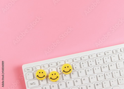  flat lay of threes yellow circle smiling faces on white computer keyboard on pink background.