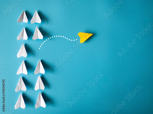 Yellow paper airplane origami leaving other white airplanes on blue background with customizable space for text. Leadership skills concept photo