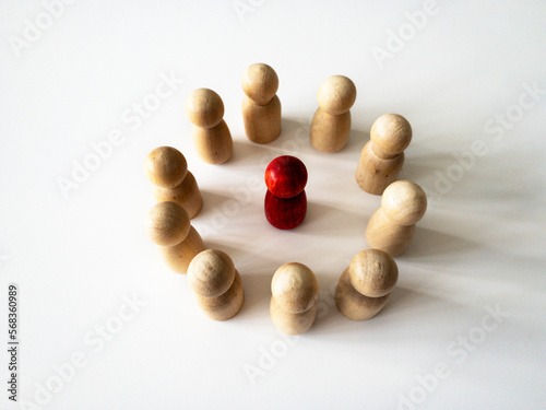 Red wooden doll figure surrounded by other doll figure on white background. Harassment and bully concept.