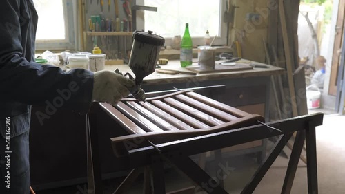 Slow motion. Carpenter-men wearing gloves, apply varnish or primer with compressed air on a wooden surface. Painting of wooden products with a spray gun in a carpentry workshop at a furniture factory