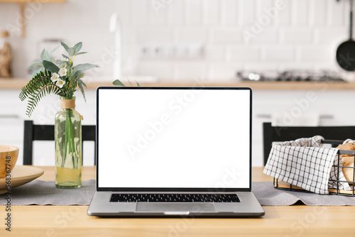 фотографія Modern computer, laptop with blank screen on table with blur modern kitchen back
