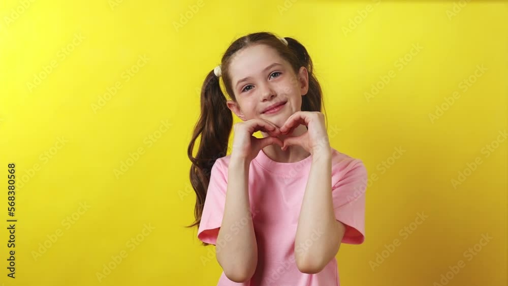 Beautiful little girl shows her heart with her hands and sends an air kiss on a yellow background, 4K Beautiful little girl shows her heart with her hands and sends an air kiss on a yellow background, 4K