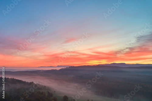 Foggy landscape at sunrise. Range of hills in front of agricultural fields. Blue sky with red accents. Fog in the valley in the autumn season. Aerial view with drone. Germany, Nurtingen, Swabian alb.