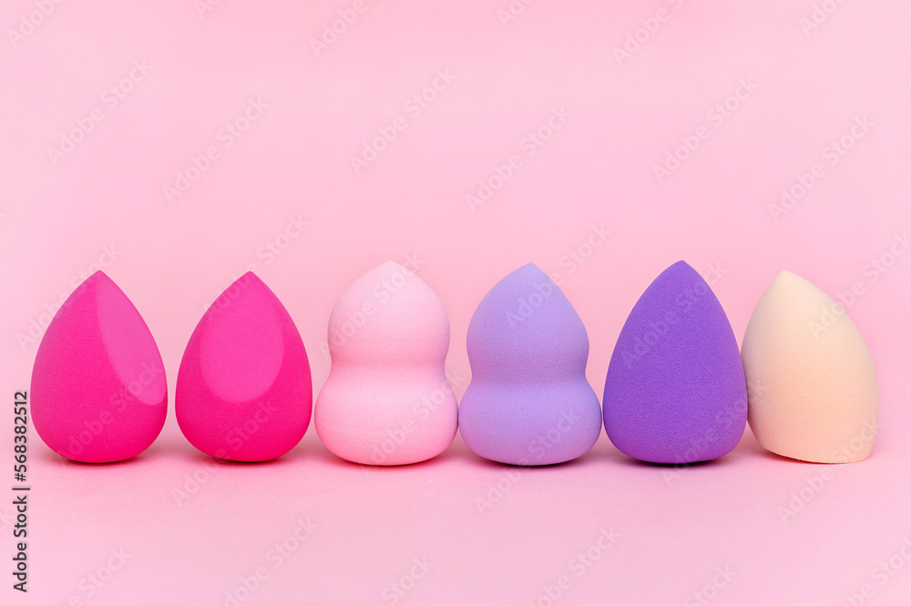 Makeup sponges of different shapes and colors on a pink background
