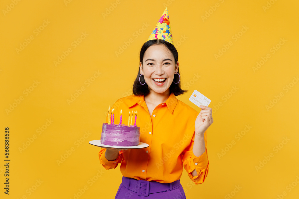Happy fun surprised shocked young woman wears casual clothes hat celebrating hold in hand cake with candles credit bank card isolated on plain yellow background. Birthday 8 14 holiday party concept. Happy fun surprised shocked young woman wears casual clothes hat celebrating hold in hand cake with candles credit bank card isolated on plain yellow background. Birthday 8 14 holiday party concept.