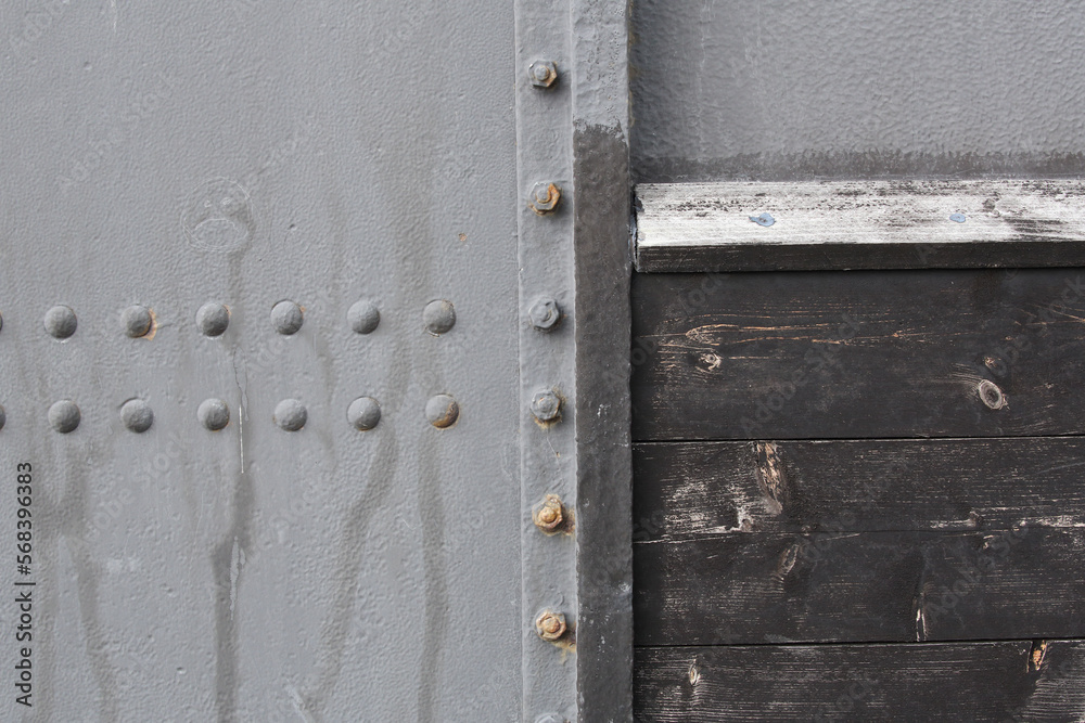 A close-up of metal plates and a wooden panel. The plates are attached with rivets and bolts.
