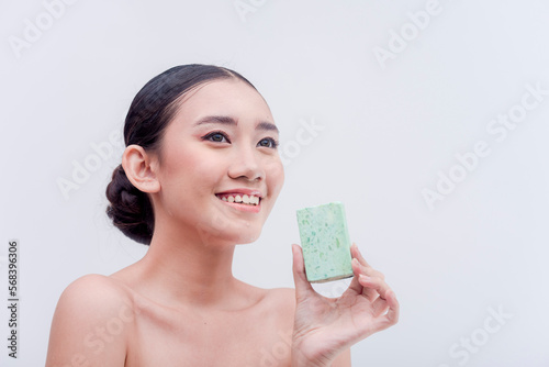 Asian female beauty products endorser smiles while holding a bar of facial soap. Skin care products for hydrating, moisturizing, glowing, and whitening. Studio shot with white background.