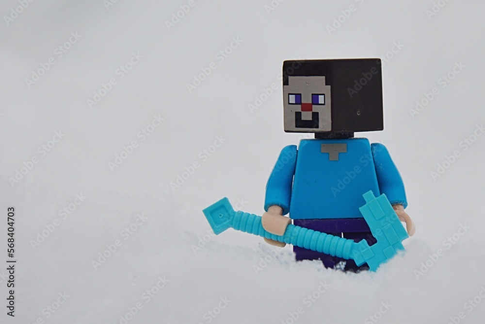Fototapeta premium LEGO Minecraft smiling figure of Steve standing with his diamond pickaxe in deep snow.