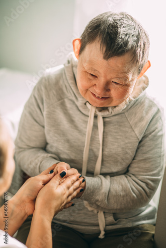 an elderly woman with Down syndrome, accompanied by an assistant who supports her, holds her hands