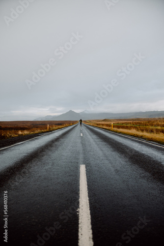 Road landscape in Iceland with person at the end running with mountains background in brown and gray colors.