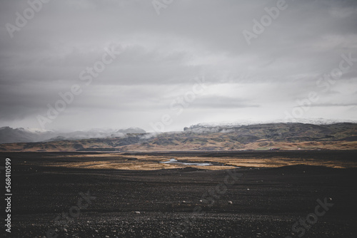 Iceland landscape with black and brown soil on a plateau with mountains and glacier in the background