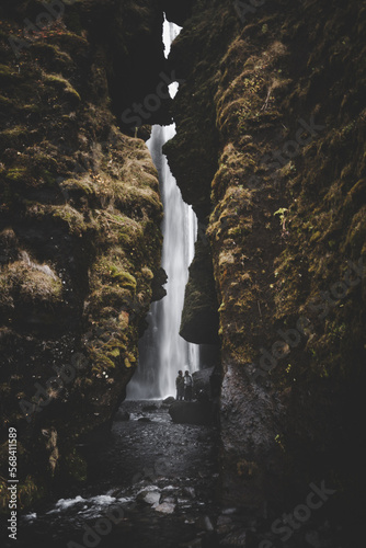 Grotto of a waterfall in iceland with walls covered in moss and two people in the background by the water