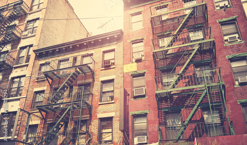 Old brick townhouses with fire escapes, color toning applied, New York City, USA.