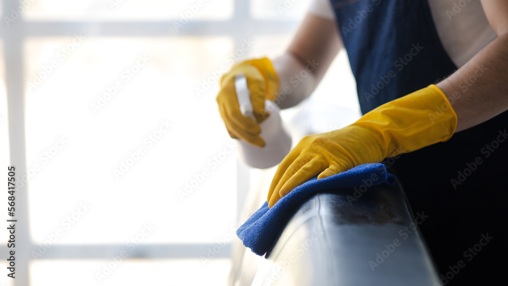 Person cleaning the room, cleaning staff is using cloth and spraying disinfectant to wipe the sofas in the company office room. Cleaning staff. Maintaining cleanliness in the organization. Person cleaning the room, cleaning staff is using cloth and spraying disinfectant to wipe the sofas in the company office room. Cleaning staff. Maintaining cleanliness in the organization.