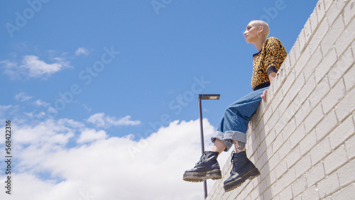 A beautiful woman with leopard print clothing sitting on a wall with a blue sky overlooking city