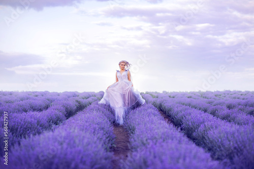beautiful woman in a lush long dress runs in a lavender field. A girl in the image of a fairy and a princess of flowers.
