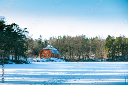 Traditional idyllic Swedish red wooden timber cabin house paint with falu red paint in winter landscape by frozen lake photo