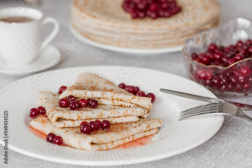 Russian traditions. Russian holiday Maslenitsa. Still life with a cup of tea, a stack of pancakes with northern cranberries, cubes of butter on the table.