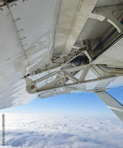 Detailed view of flaps , high-lift devices and actuators of a general aviation airplane flying at stall speed. Strut and wing of semi-cantilever high-wing aircraft over the clouds on a sunny day.