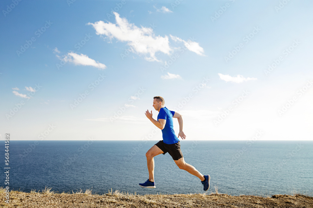 man mature runner running trail in background blue sky and sea