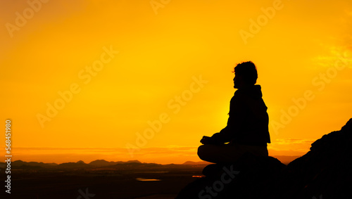 Silhouette of a person in the lotus position with orange sky and mountains in the background. Concept meditating at sunrise. Copy space on the right