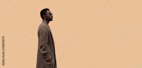 Fashionable portrait of stylish african man model looking away wearing knitted cardigan isolated on brown background, profile view, blank copy space for advertising text
